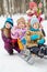 Girl pushes sled with two children, another one girl stands behind