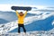 Girl raises snowboard up against panoramic winter mountain