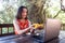 A girl in a red dress communicates with relatives via the Internet on the veranda of a wooden house