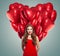 Girl in red dress with heart balloons. Beautiful woman with red lips makeup, perfect curly hair and cute smile.