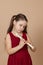 Girl in red dress learn melody by pinching holes in flute with bowed head, beige background. Tuition to play woodwind