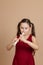 Girl in red dress play with pleasure melody on flute, blowing air into duct, beige background. Learn to play woodwind