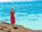 Girl in a red dress on a rock in the background of the sea landscape, Cook Islands, South Pacific. With selective focus. Back view