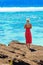 Girl in a red dress on a rock in the background of the sea landscape, Cook Islands, South Pacific. With selective focus. Back view