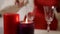 A girl in a red dress sits at a table by candlelight and drinks champagne from a glass