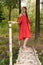 A girl in a red dress is standing on a wooden bridge in the forest