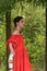 A girl in a red dress is standing on a wooden bridge in the forest