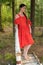 A girl in a red dress is standing on a wooden bridge in the forest