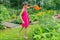 A girl in a red dress with a watering can in her hands watering flowers on a flower bed in the garden.