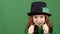 Girl red hair celebrating saint patrick`s day green wall background eating vegetable