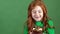 Girl red hair celebrating saint patrick`s day green wall background looking on pot with gold