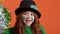 Girl red hair celebrating Saint Patrick`s Day orange background dancing with pom poms