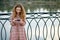 A girl with red hair in a checkered dress stands on the embankment and looks at her phone in a funny video