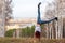 A girl with red hair makes an acrobatic wheel on nature against the background of a blurred city and forest.