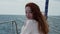 A girl with red hair sits on the bow of a yacht that rides along the sea Smile and look at you
