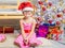 Girl in the red hat and the funny round glasses sits on the mat at the Christmas trees