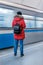 A girl in a red jacket with a backpack stands with her back on the Moscow subway platform against the background of the departing