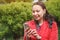 Girl in a red jacket in the Park listening to music with headphones earbuds with a smartphone in hand