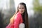 A girl in a red jacket and white jeans sits and poses in a city park