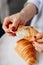 A girl with a red manicure tears a French croissant. The layers are torn apart