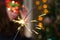 Girl in a red mask near a Christmas tree with sparkler.