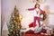 Girl in red pajamas with deer jumps on bed next to Christmas tree
