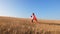 Girl in red raincoat plays superhero in field with wheat. Slow motion