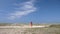 A girl in a red skirt walks on the sandy ground against the backdrop of an endless blue sky