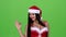 Girl in the red suit of the santa woman winks and shows her finger ok. Green screen. Close up