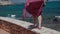 Girl in a red summer dress runs barefoot on a stone fence along the seafront. Rear view. Close-up of female legs