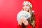 A girl in a red sweater and a Santa hat, holds the money and looks away thinking where to spend it on a red background