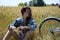 Girl relax with bicycle on summer meadow. Young woman sit at bicycle on country road. Pretty young woman with bicycle in summer.