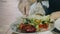 The girl in the restaurant eating a salad of vegetables from a white plate. In the hands of girls the silver a fork. Close-up of a