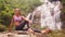 Girl rests sitting on stone in front of waterfall in jungle