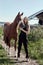 Girl rider stands next to the horse in the field. Fashion portrait of a woman and the mares are horses in the village in the grass