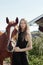 Girl rider stands next to the horse in the field. Fashion portrait of a woman and the mares are horses in the village in the grass