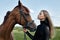 Girl rider stands next to the horse in the field. Fashion portrait of a woman and the mares are horses in the village in the grass