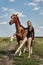 Girl rider stands next to the horse in the field. Fashion portrait of a woman and the mares are horses in the village in the grass