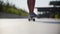 Girl rides a skateboard past the camera, in the frame of the legs in sneakers