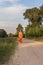 A girl in a rural summer long dress walks barefoot along a country sandy road at sunset in the village