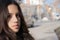 Girl`s face side view grey eyes dark brown hair blurry street with cars