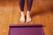 The girl& x27;s feet stand in front of an unfolded Yoga mat on the wooden floor.