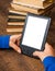 Girl`s hands hold E-book on mobile device above pile of old paper book with blank white screen on a wooden background