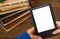 Girl`s hands hold E-book on mobile device above pile of old paper book with blank white screen on a wooden background