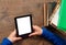 Girl`s hands hold E-book on mobile device above pile of old paper book with blank white screen on a wooden background