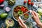 Girl`s hands taking photo of Buddha bowl salad with chickpeas, quinoa, tomatoes, arugula, avocado, sprouts by smartphone. Healthy