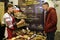 Girl sales manager in Ukrainian national costume holding a piece of bread proposing to buy to a man customer, bakery