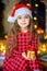 Girl in santa claus hat sits on the floor with a gift in hands