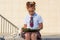 A girl in school uniform with a funny hairdo with colored pencils in her hair and with books sits on the steps in front of the
