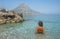 Girl in the sea with clear transparent azure water. Beautiful back, tanned skin. The rocky island of Telendos, Greece